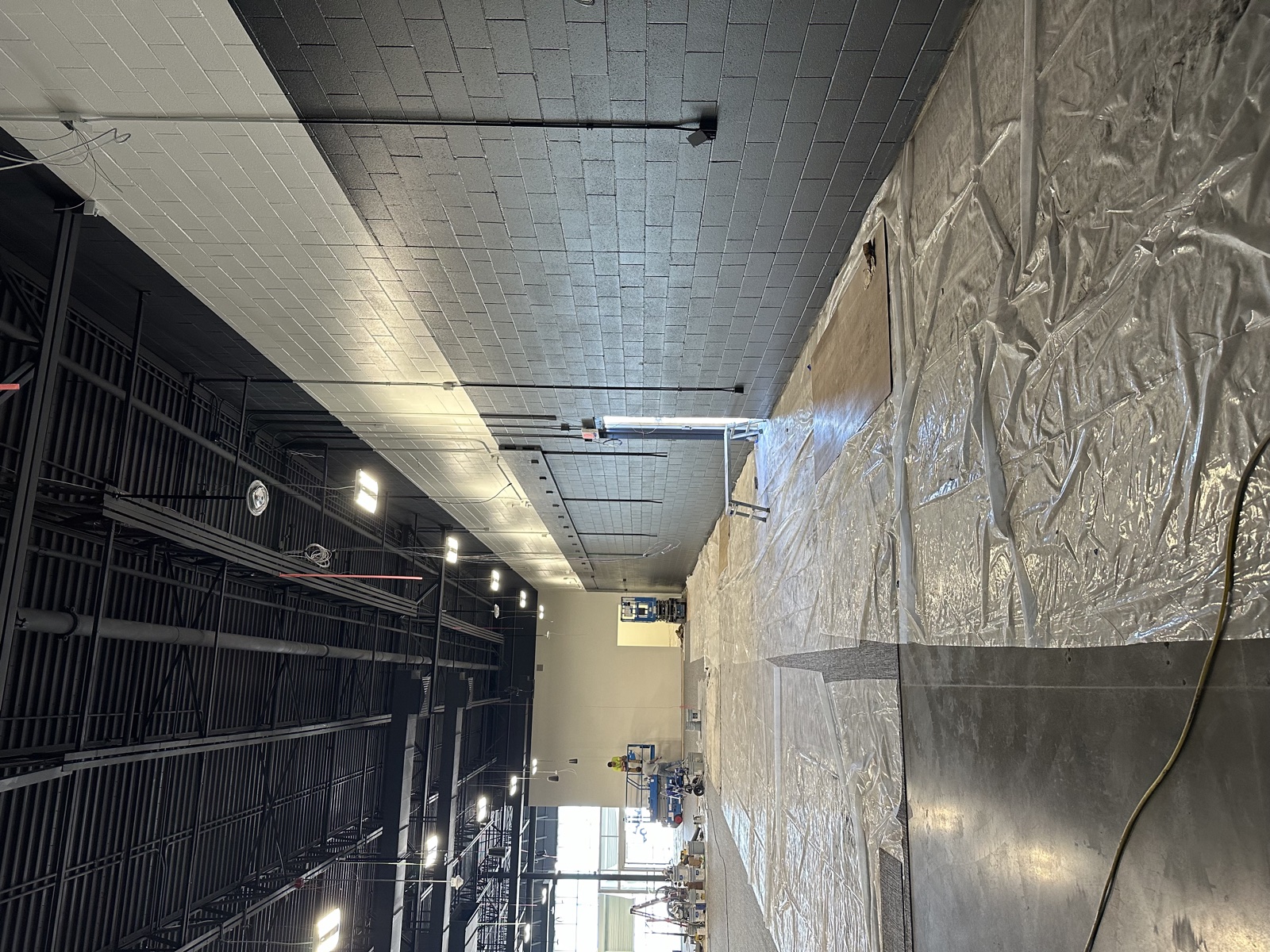 Large commercial interior with a dark drop-tile ceiling and walls being repainted black, drop cloths covering the floor, and a Silver Valley painter on a stepladder