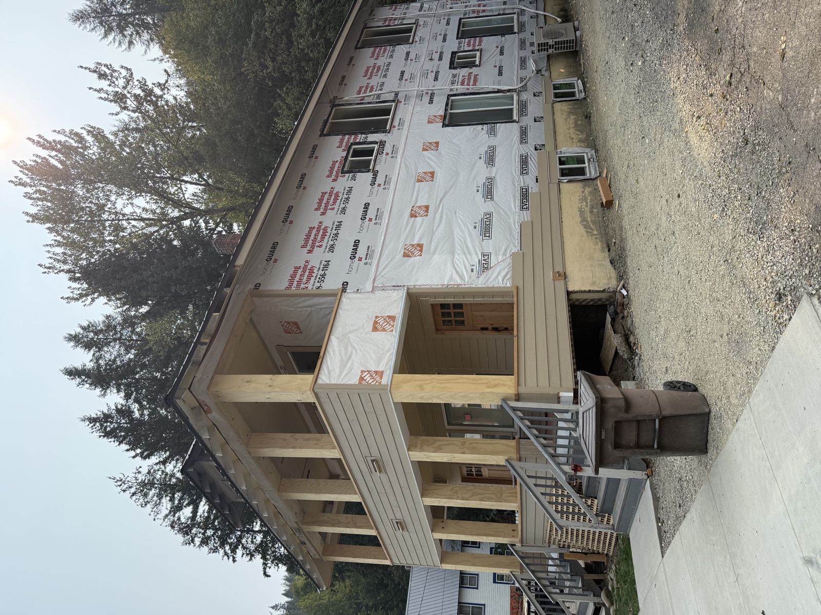 Two-story residential build at the wrap-and-frame stage with red-printed house wrap applied across the walls and a framed deck and porch structure ready for siding