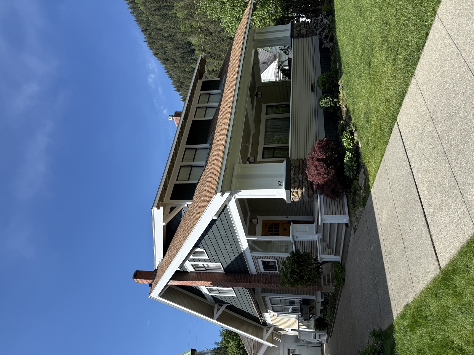 Two-tone home exterior featuring cream lower siding, gray upper accents, and a green metal roof beneath a clear blue sky