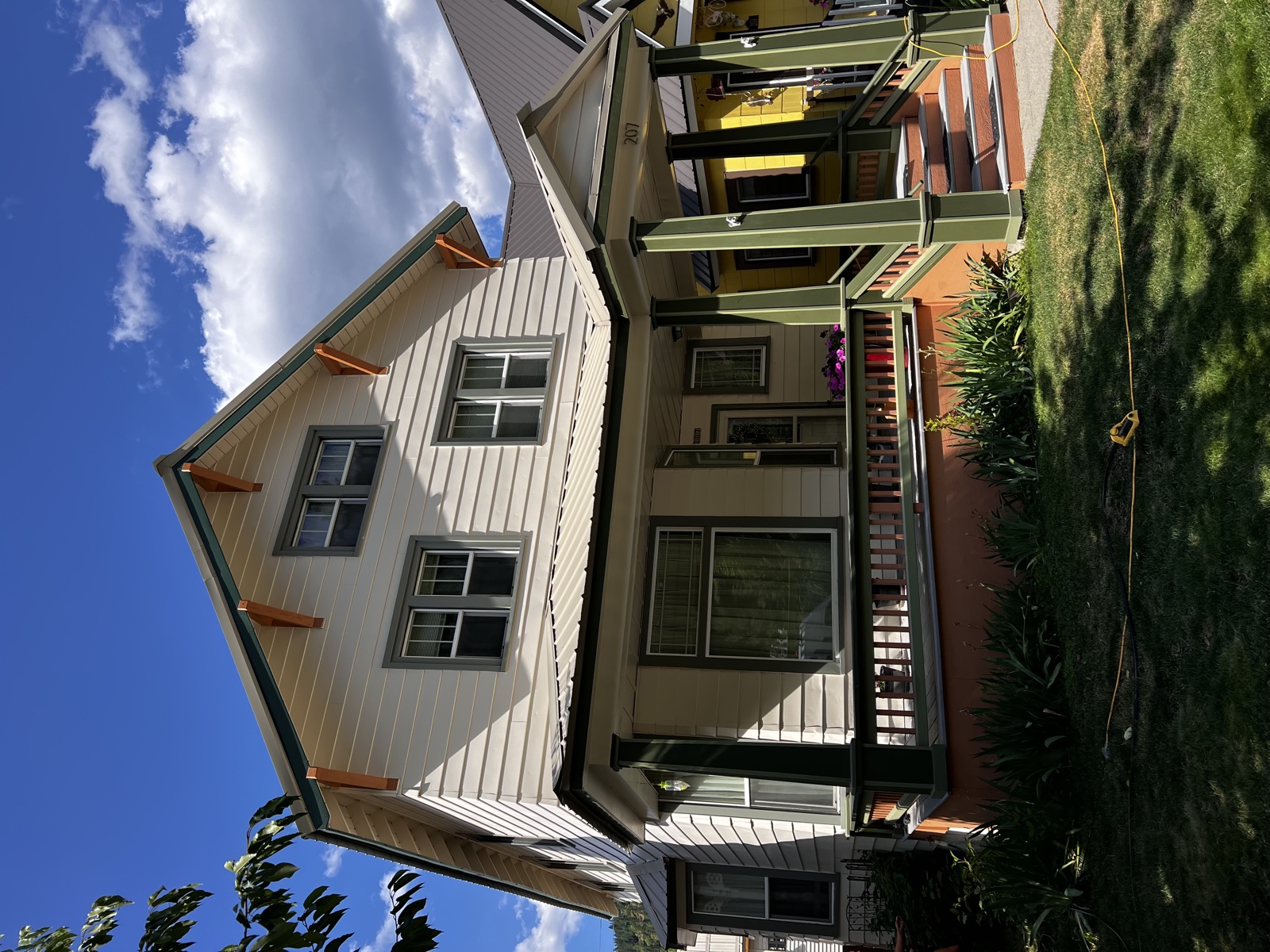 Modern farmhouse exterior with cream board-and-batten siding, dark trim, layered decks, and a green metal porch roof