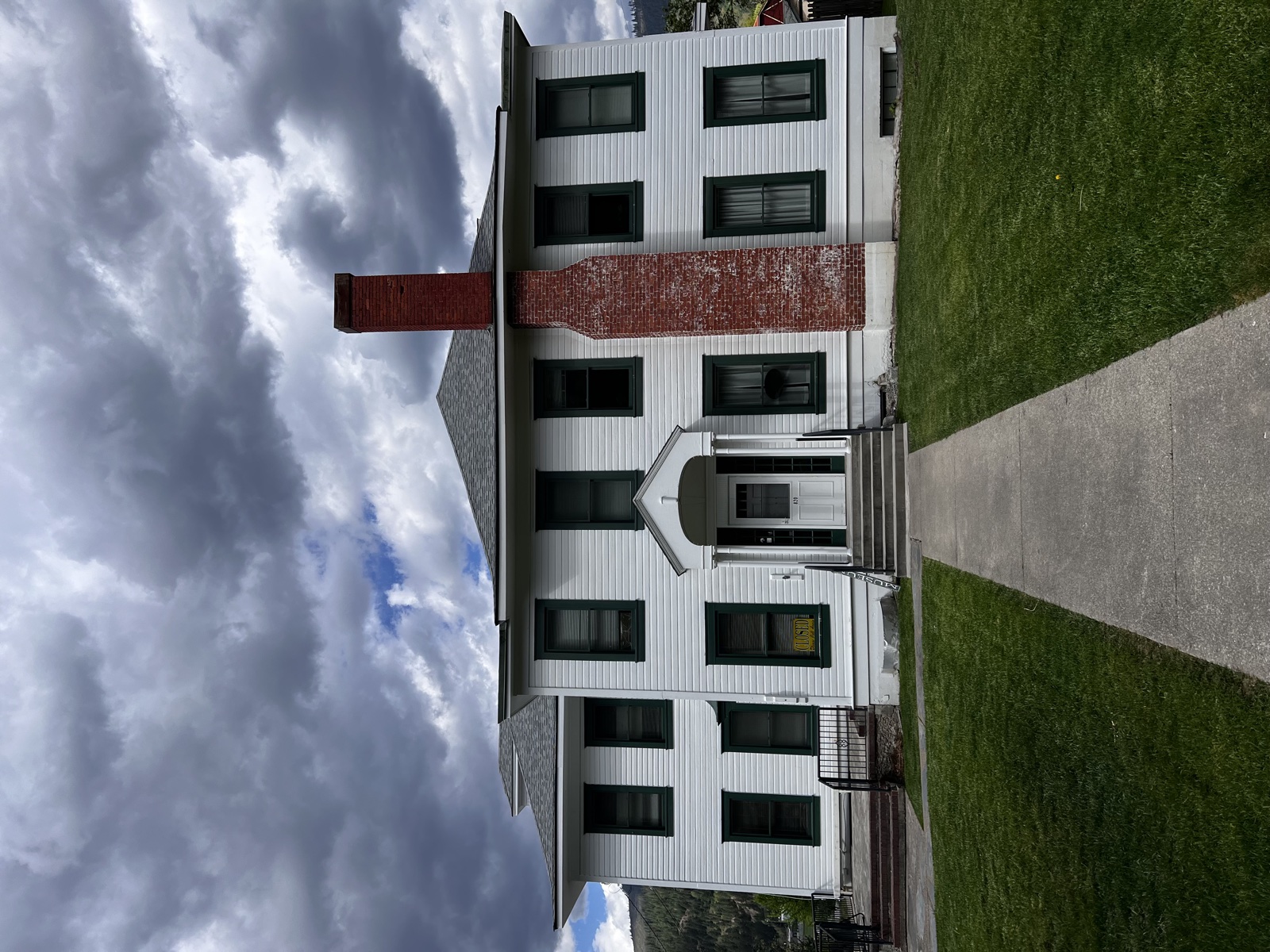 Closer view of a fresh white farmhouse exterior with central brick chimney and a covered porch beneath a cloudy sky