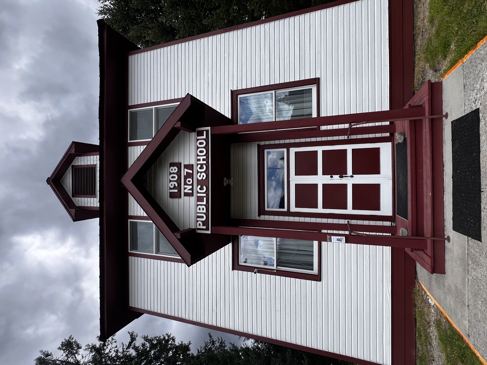Historic one-room 1908 No. 7 Public Schoolhouse repainted white with maroon trim, bell tower entry, and matching maroon double doors