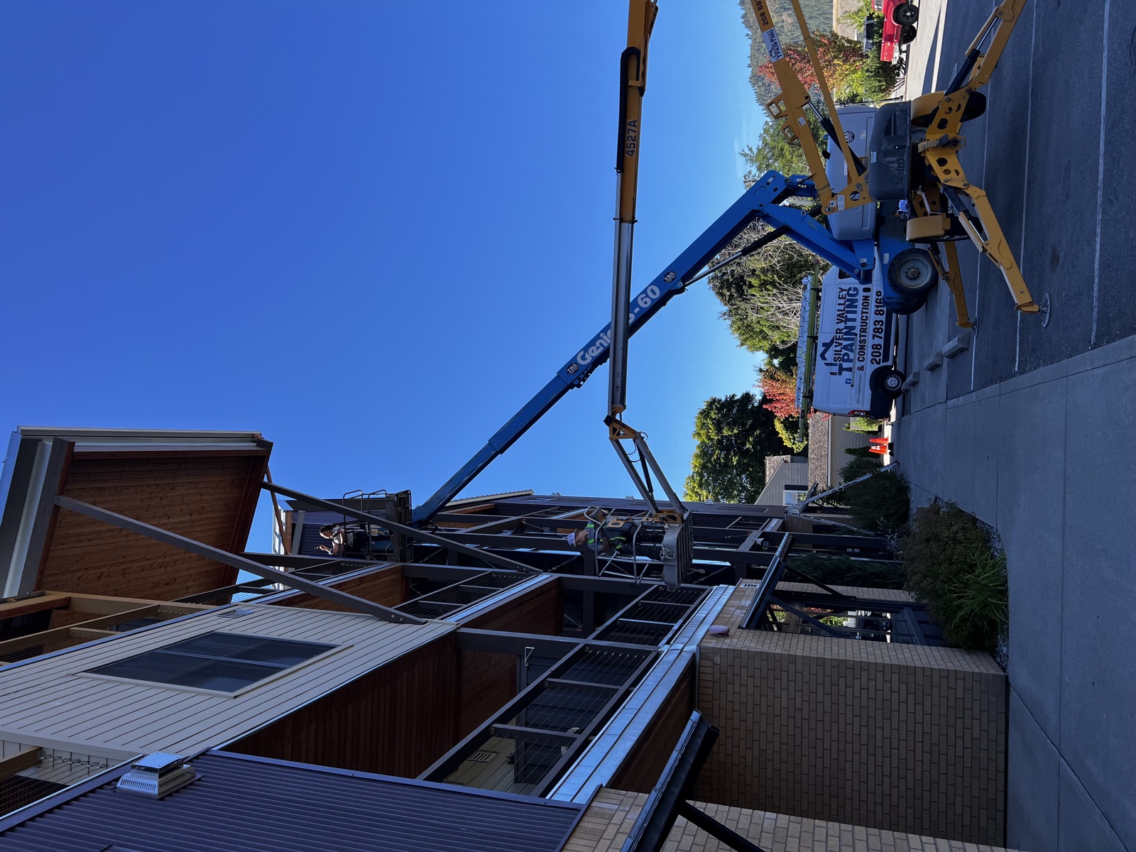 Painters on a tall blue boom lift repainting a multi-story apartment building with wood siding, mid-coat work visible against the upper floors