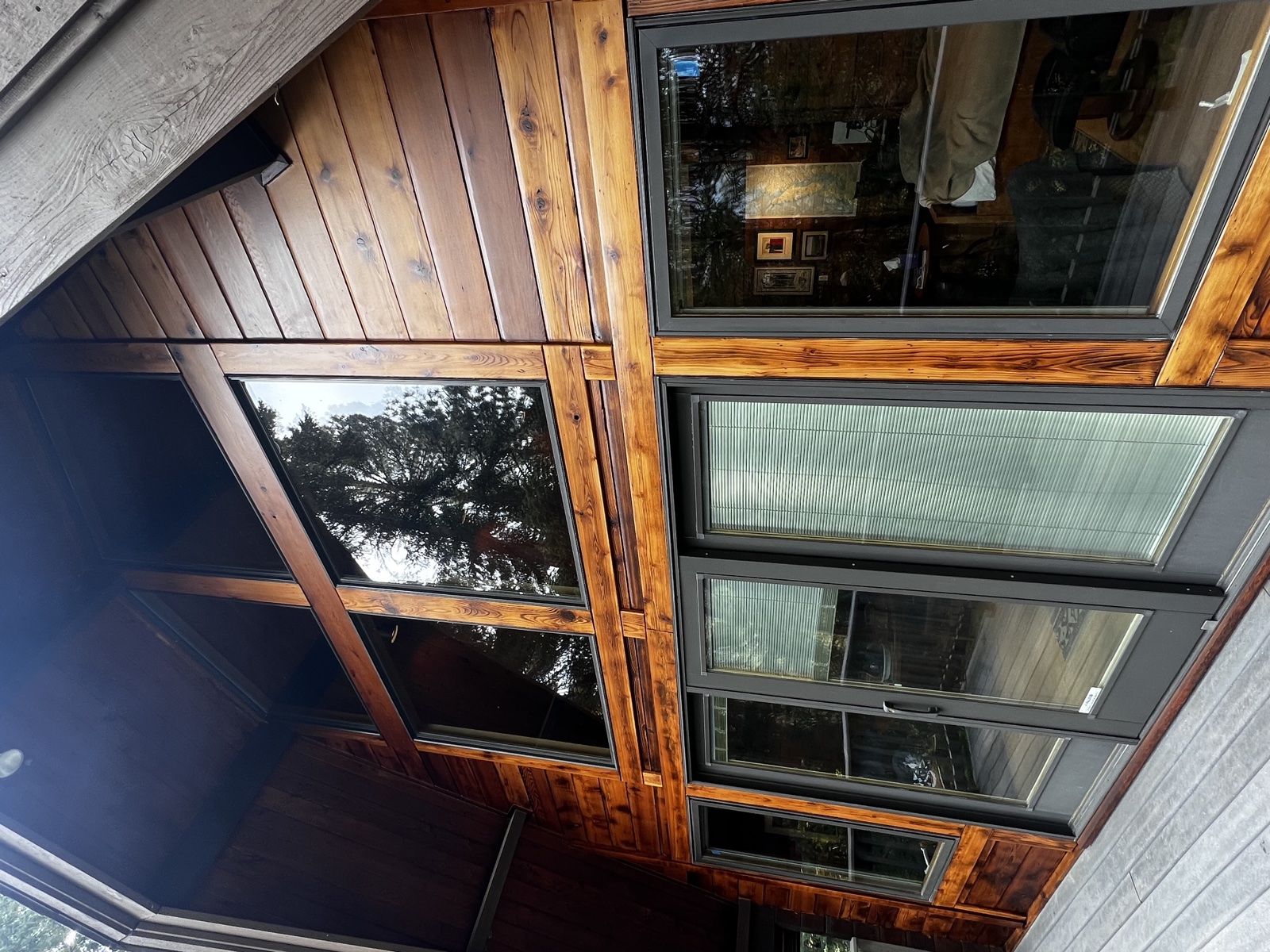 Cedar-sided cabin with restained tongue-and-groove upper siding and large picture windows, finished in a warm dark brown stain