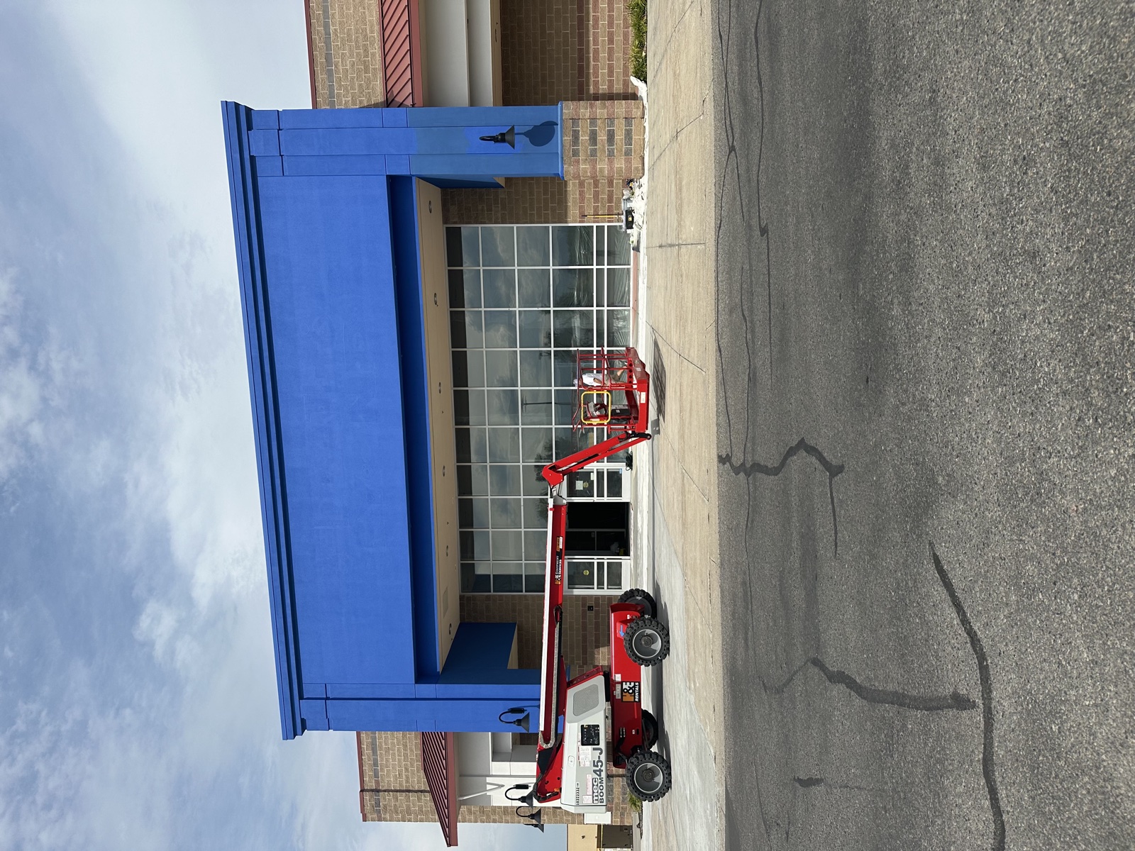 Retail storefront with a red articulating lift extended in front of a blue parapet for high exterior repainting work