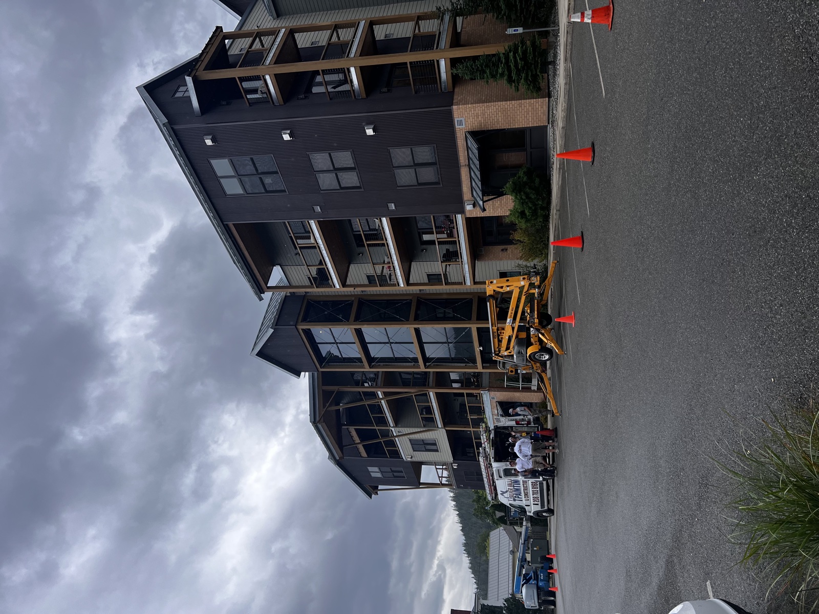 Large multi-story condominium in Wallace, Idaho with dark green metal siding and shingle accents being repainted, with an articulating lift and traffic cones in place