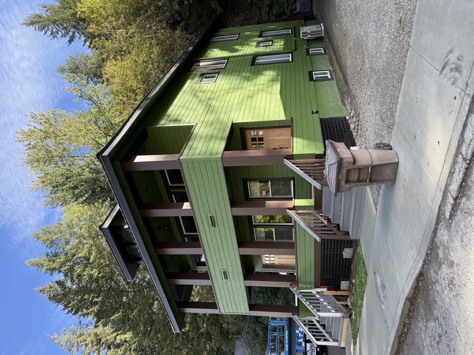 Custom-built modern home painted bright sage green with white trim, dark roof, and a cedar-stained back deck with skylights overhead