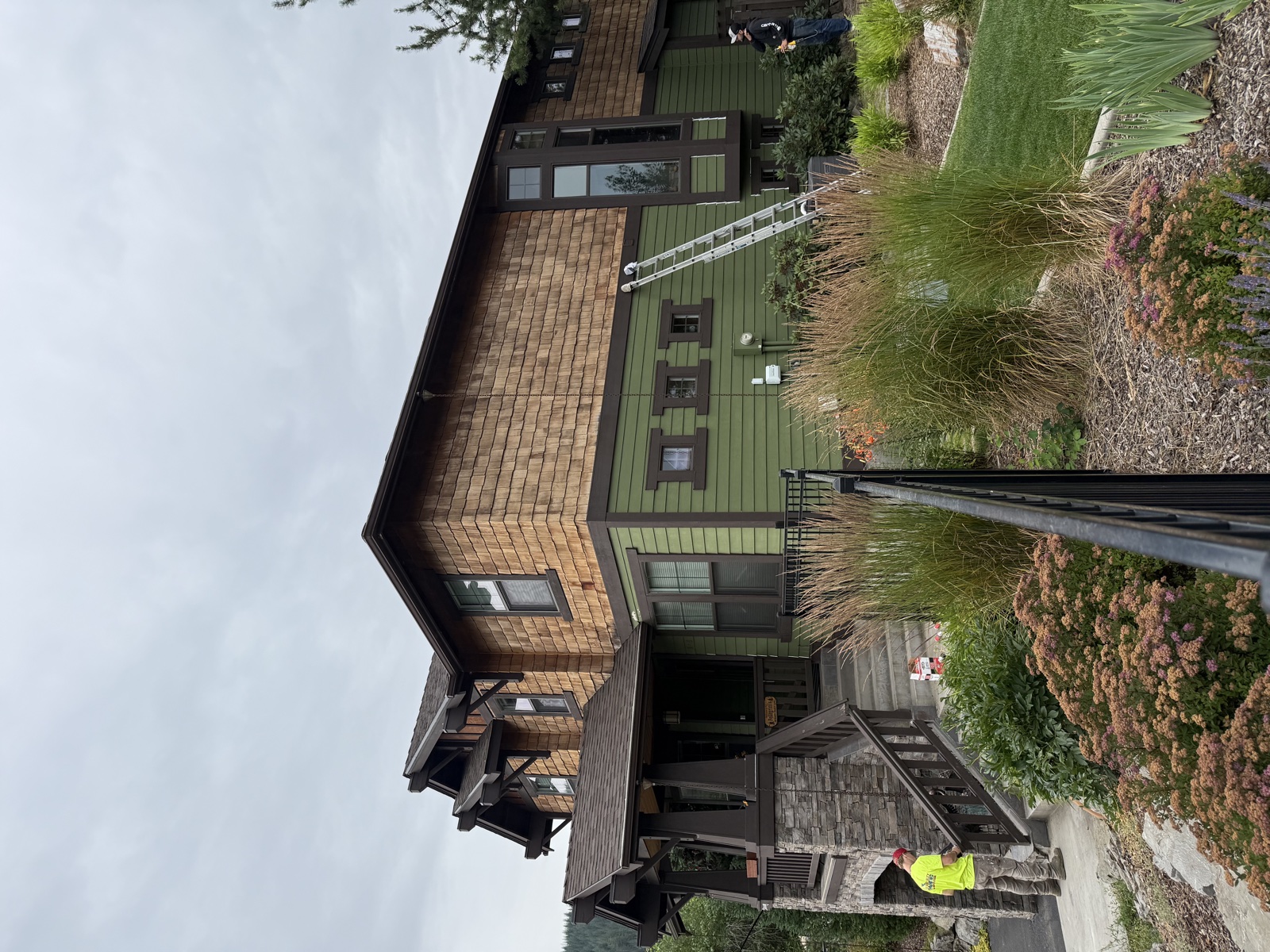 Two-story custom home repaint in Coeur d'Alene, Idaho with cedar shake accents, dark trim, and a large wooden deck wrapping the rear