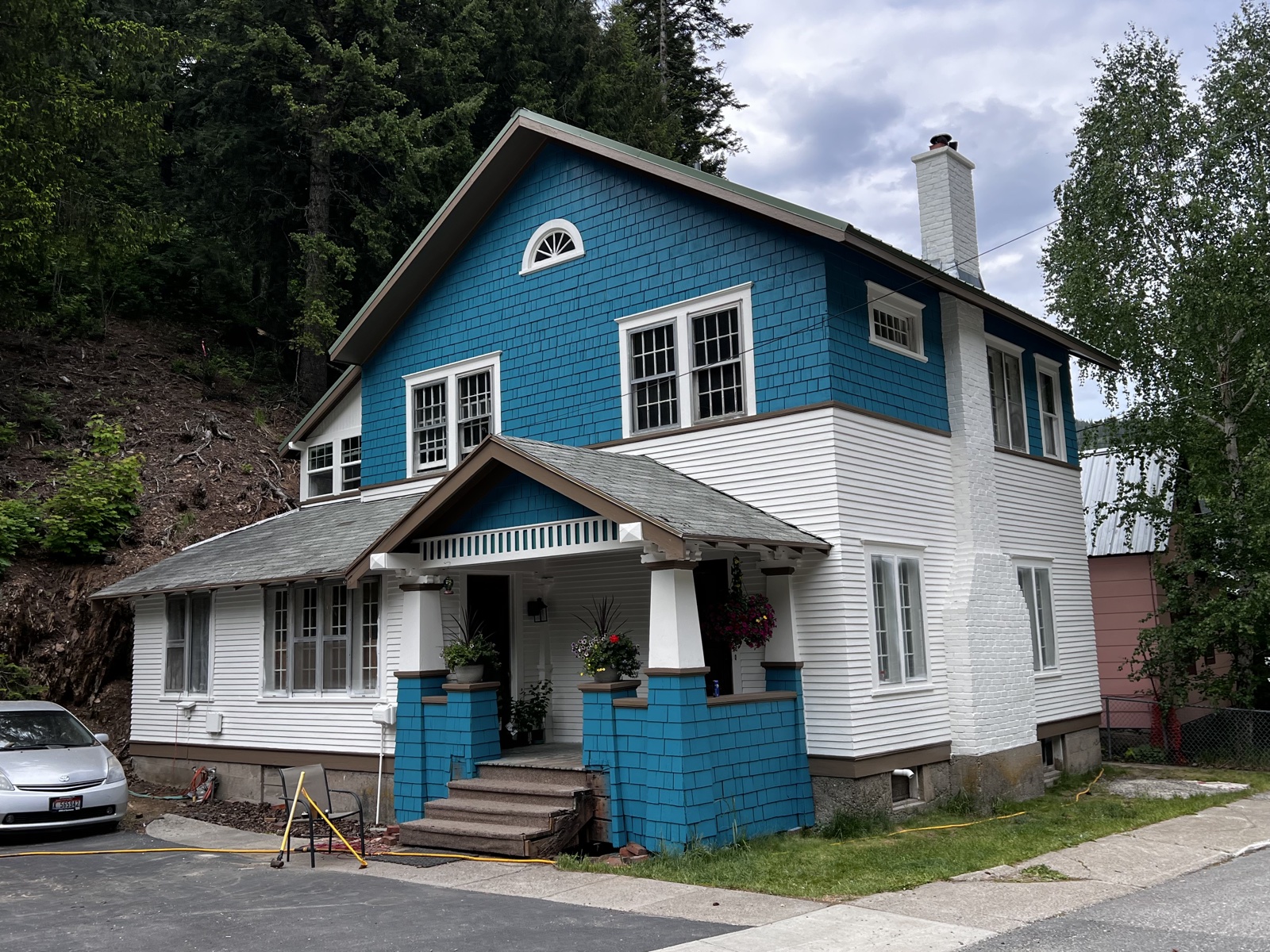 Historic blue-and-white craftsman home in Osburn, Idaho with a tall arched window detail, freshly painted shingle and clapboard siding, and white porch columns