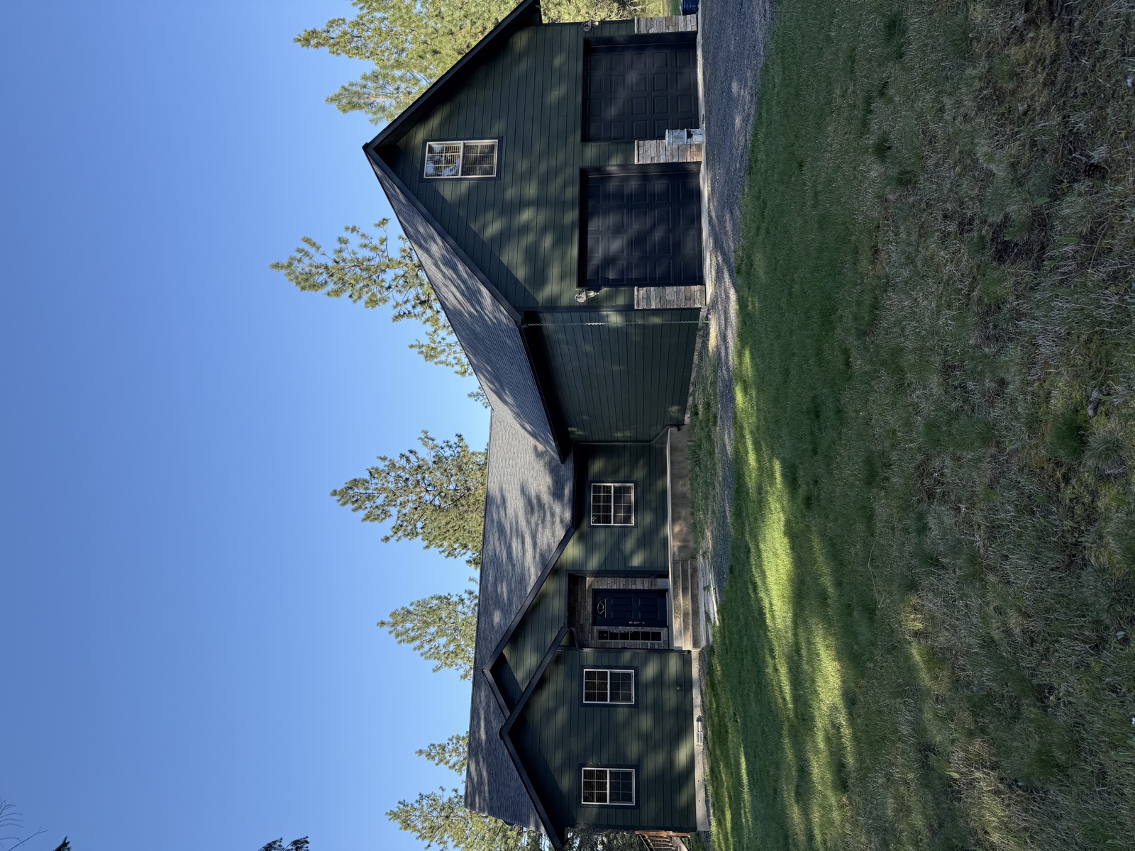 Dark forest-green barn-style outbuilding near Spirit Lake, Idaho with fresh paint, board-and-batten siding, and multiple windows under a clear blue sky