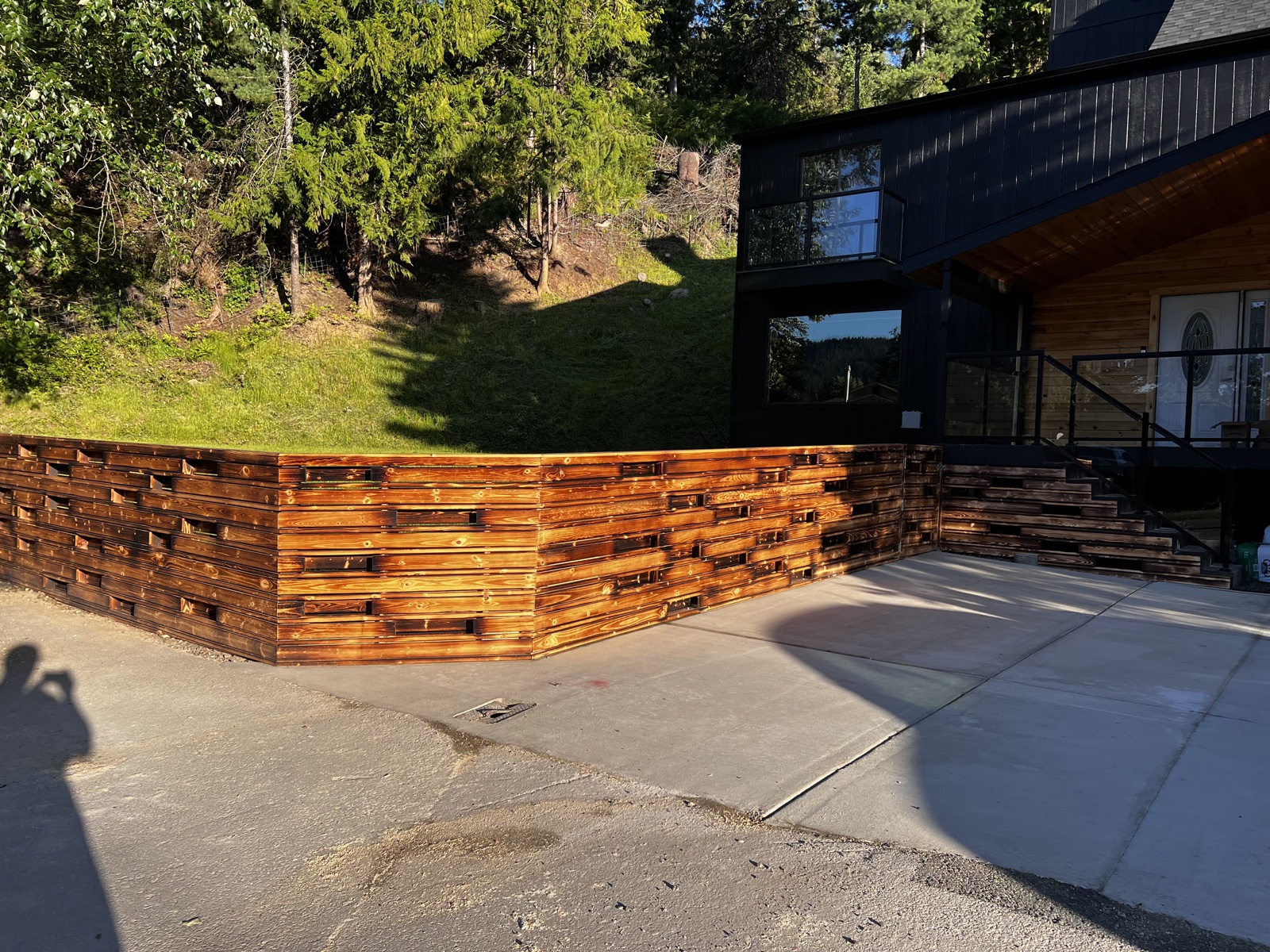 Custom horizontal woven-slat wood privacy fence freshly stained in warm honey tones, in front of a modern black home with cedar accents