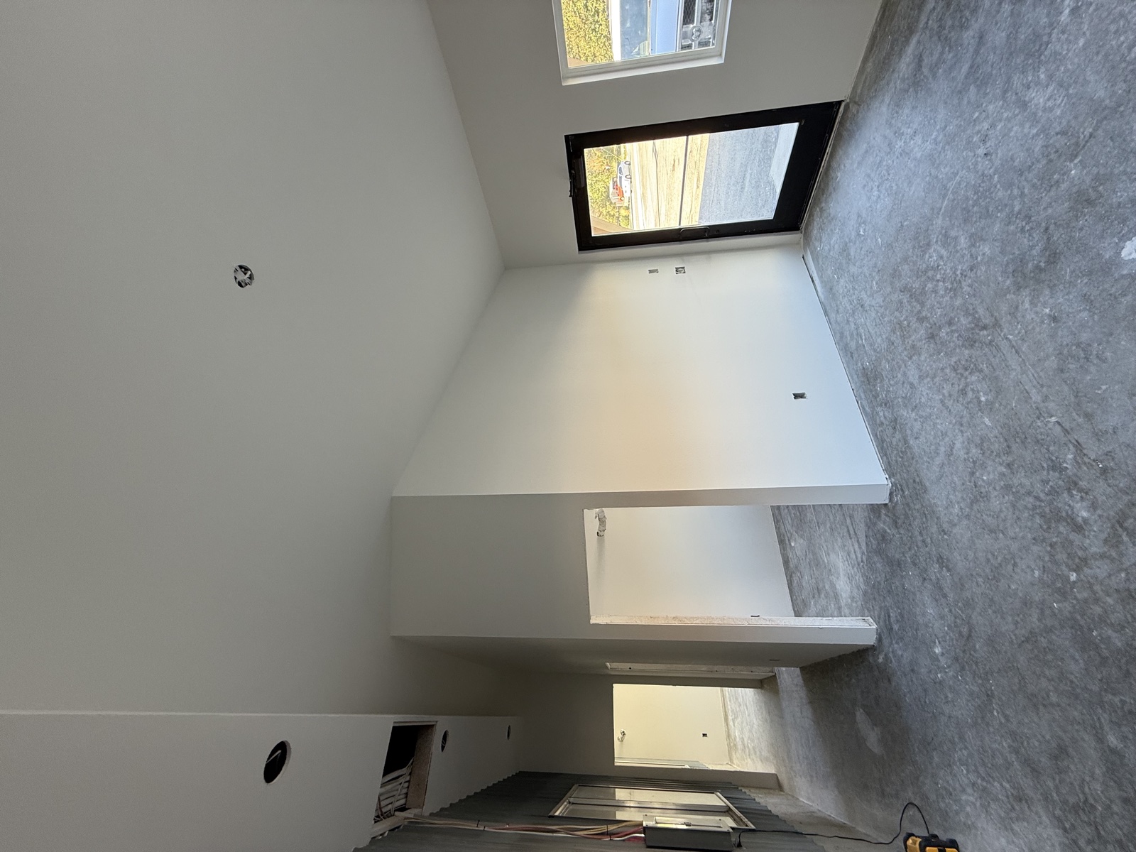 Tall vaulted white interior under final paint, with mid-finish drywall textured wall and large picture windows letting in natural light