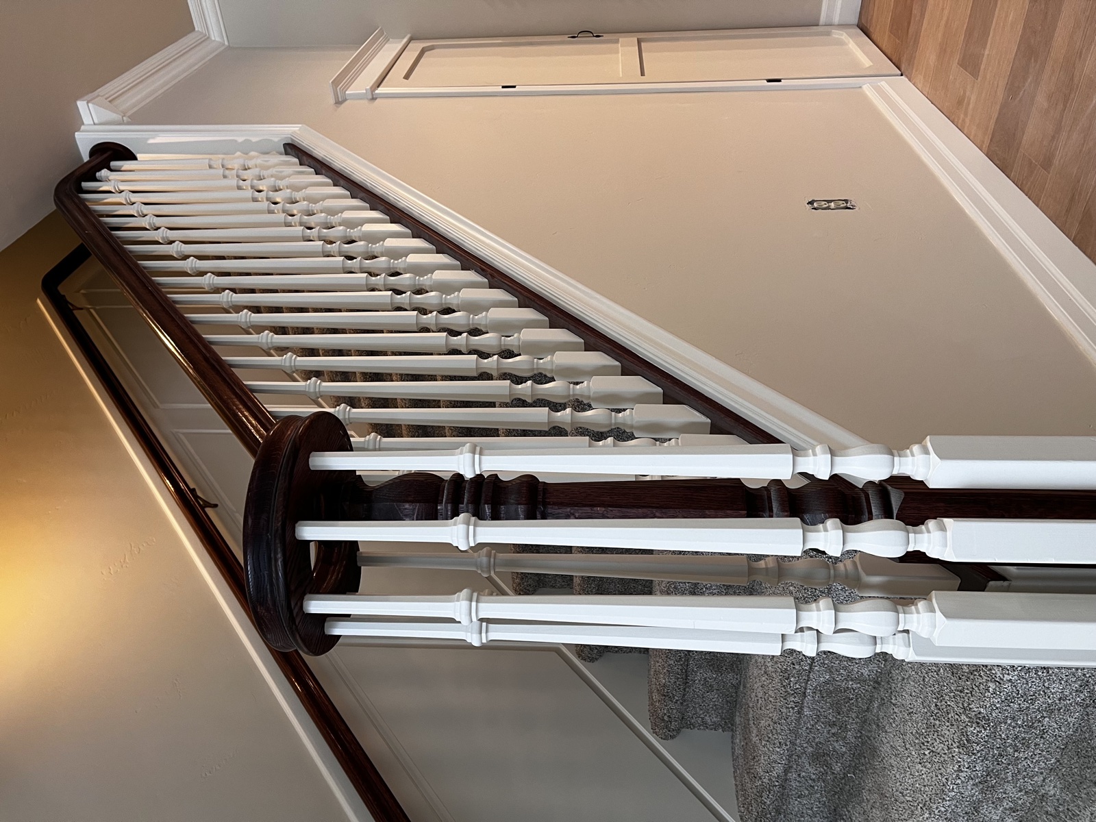 Grand interior staircase with freshly painted white turned balusters, dark stained handrails, and an ornate round newel post with carved finial