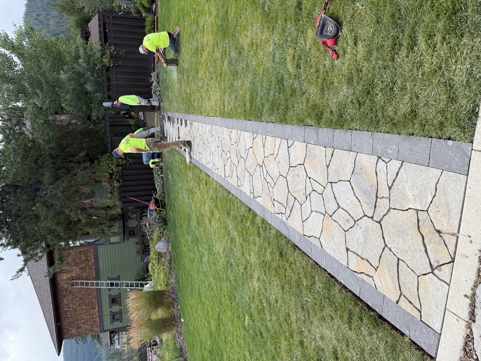 Silver Valley landscape crew in safety vests installing a wide flagstone walkway with a charcoal stone border across a residential lawn