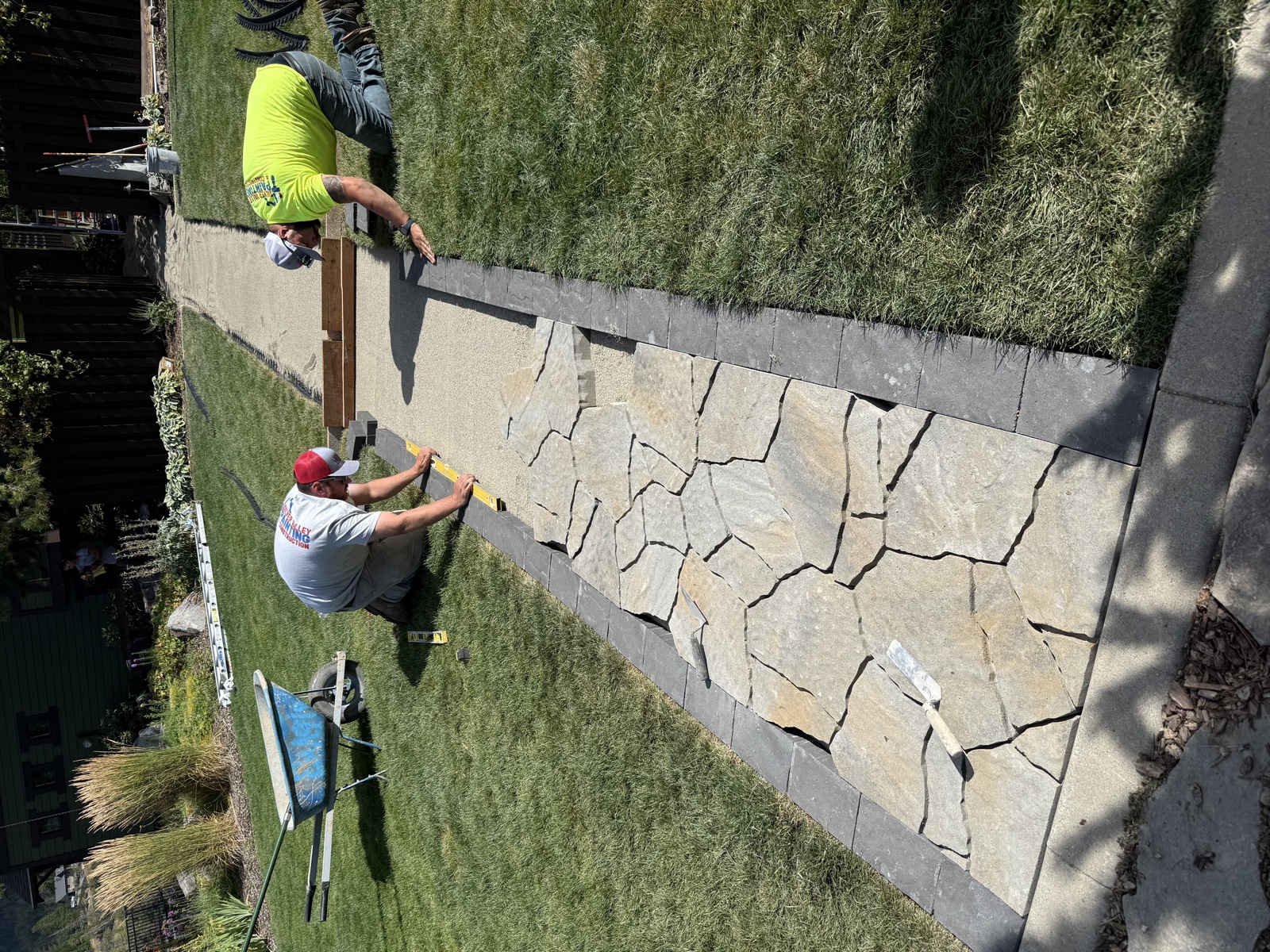 Crew member measuring and setting a long flagstone walkway with charcoal-bordered edges across a green residential lawn