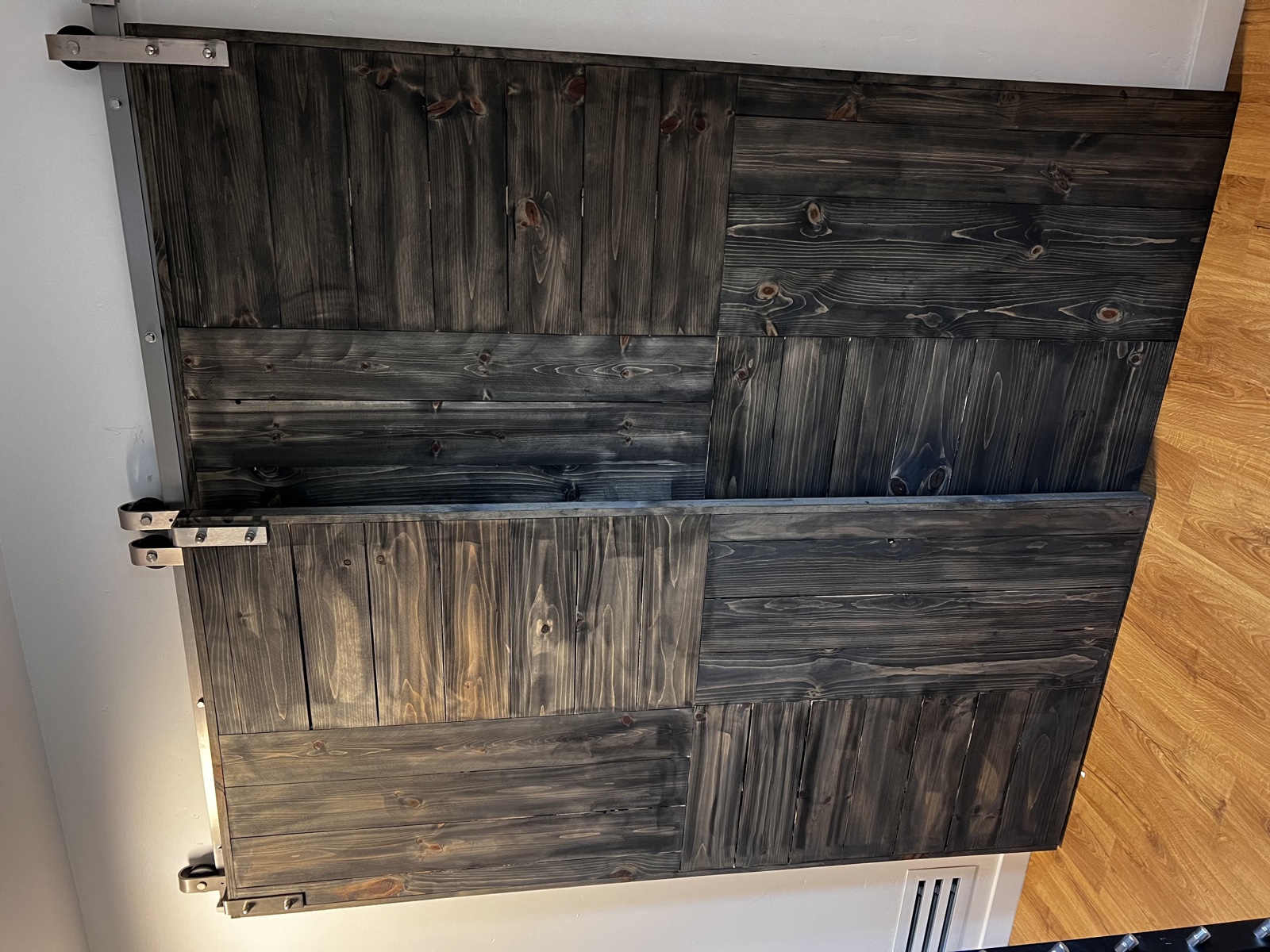 Custom dark-stained wood barn-style sliding door with checkerboard panel pattern, mounted on an exposed steel track against a light-toned wall