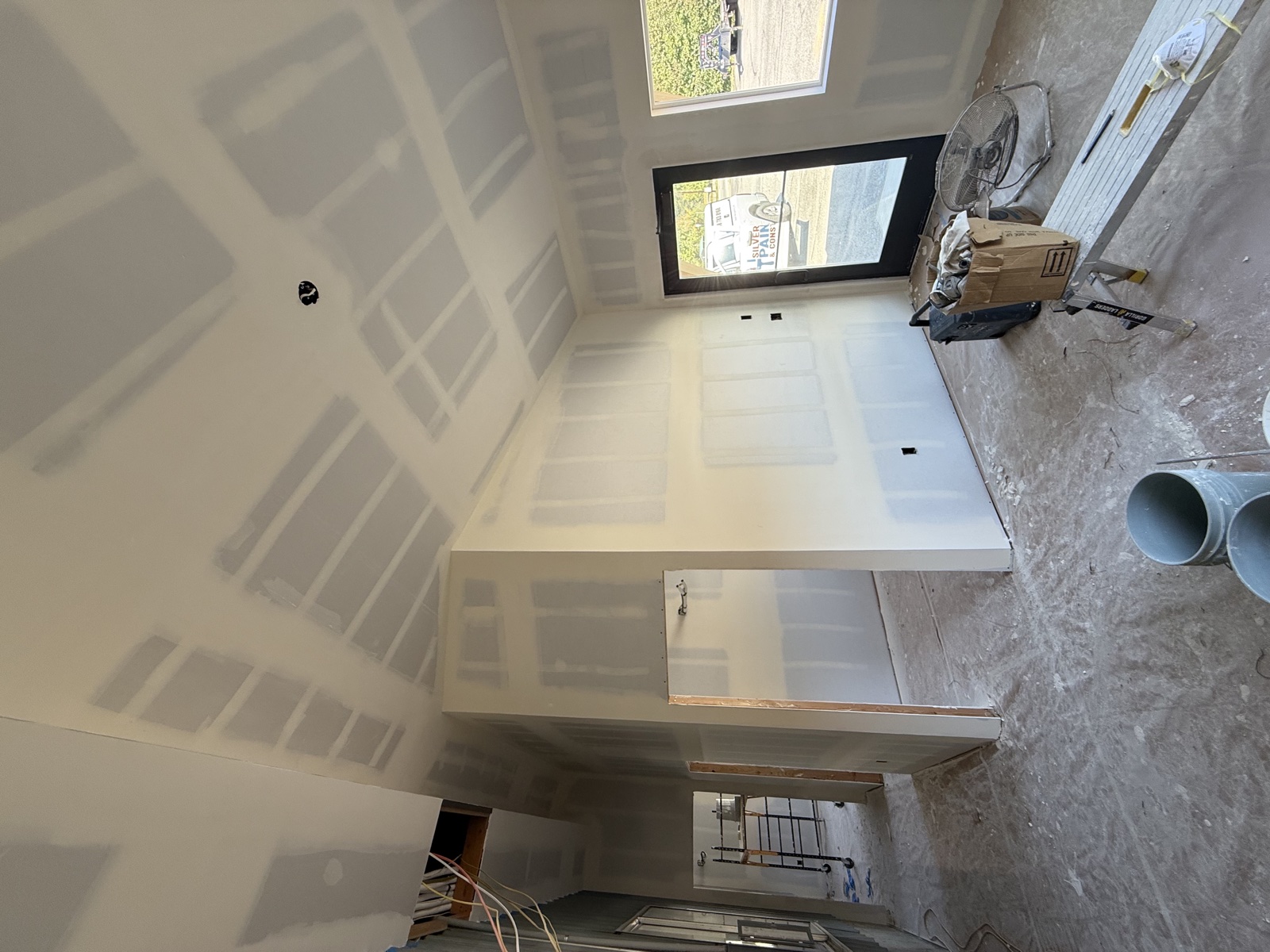 Custom remodel interior with fully drywalled walls and ceiling featuring visible mudded seams, taped corners, and a Silver Valley work van visible through the open exterior door