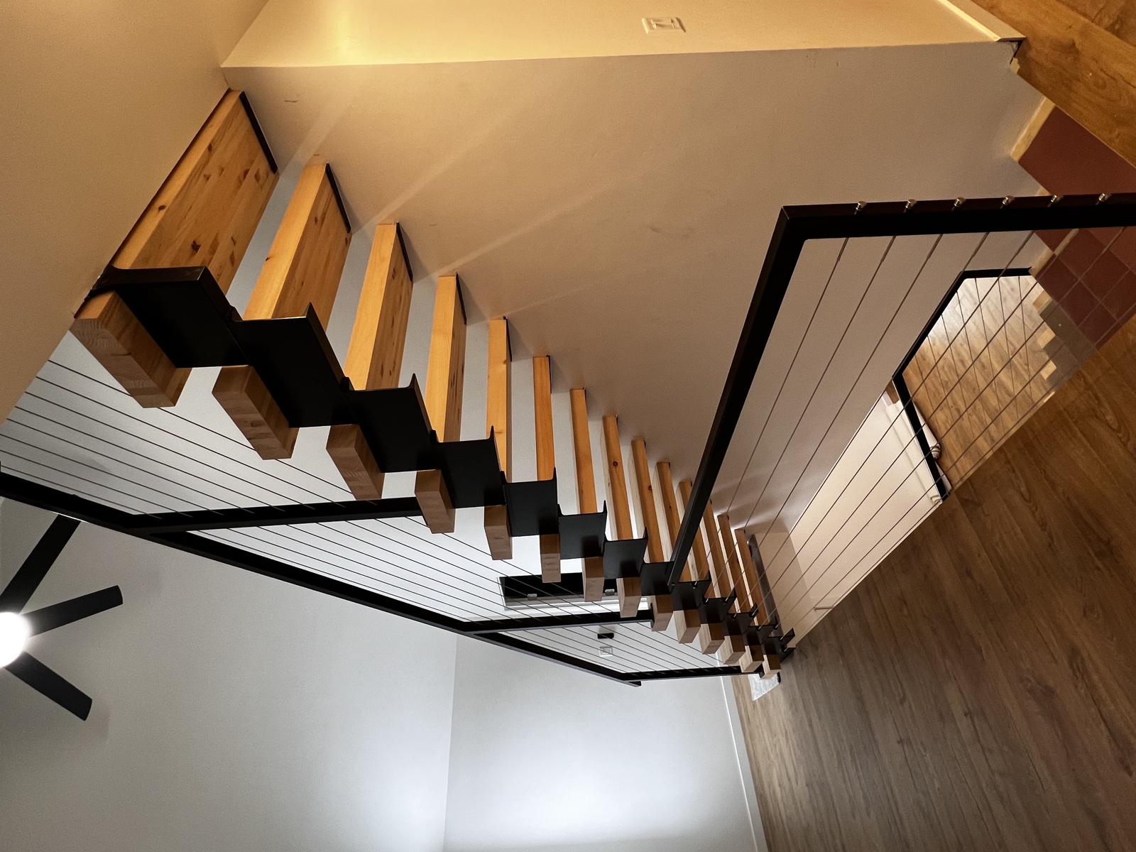 Modern floating staircase with knotty pine treads supported by black steel stringers, paired with horizontal cable railing under a vaulted white ceiling