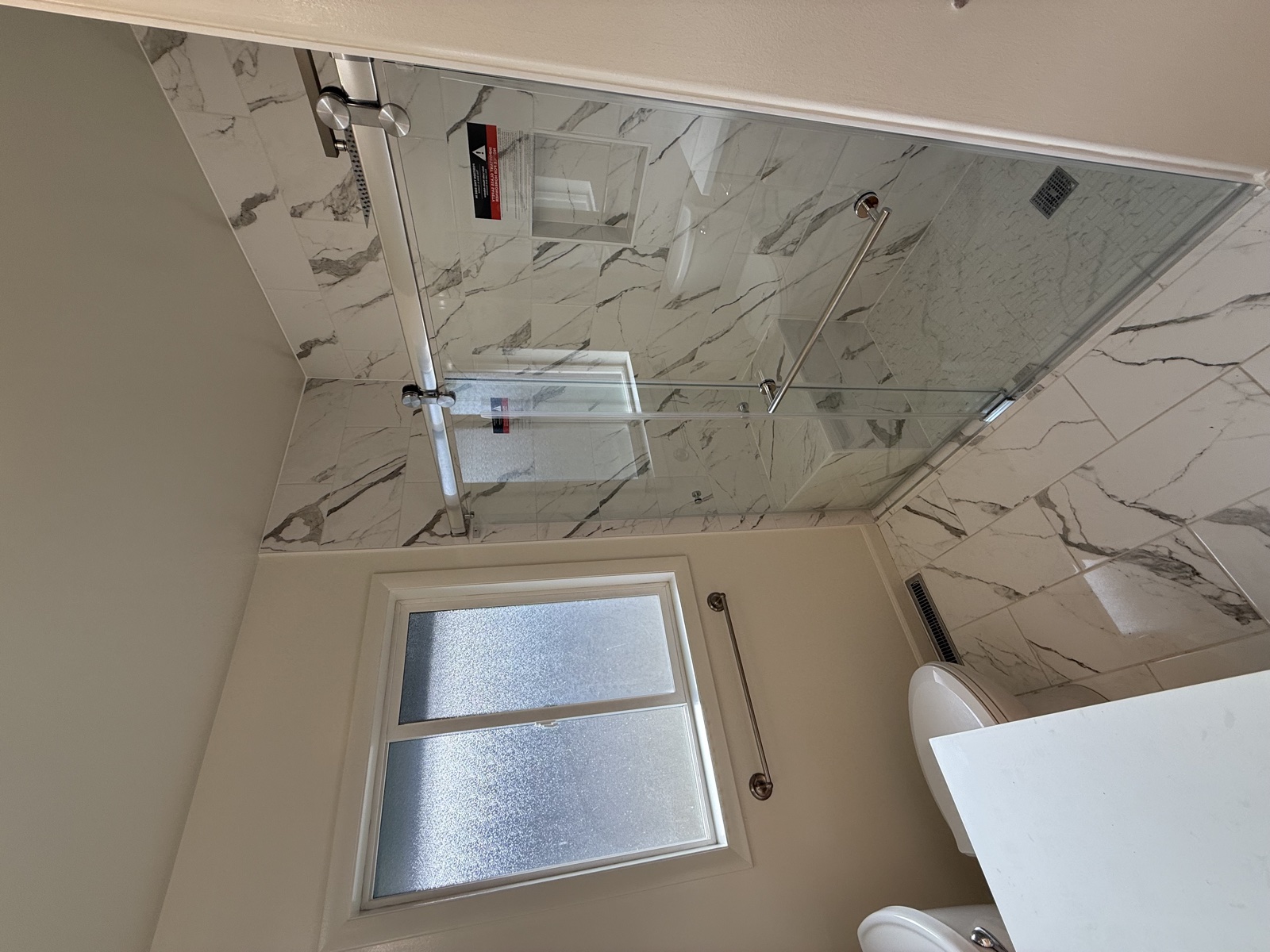 Bathroom remodel featuring a floor-to-ceiling marble slab tub surround, freestanding faucet, and a tall corner bay window above white wainscoting