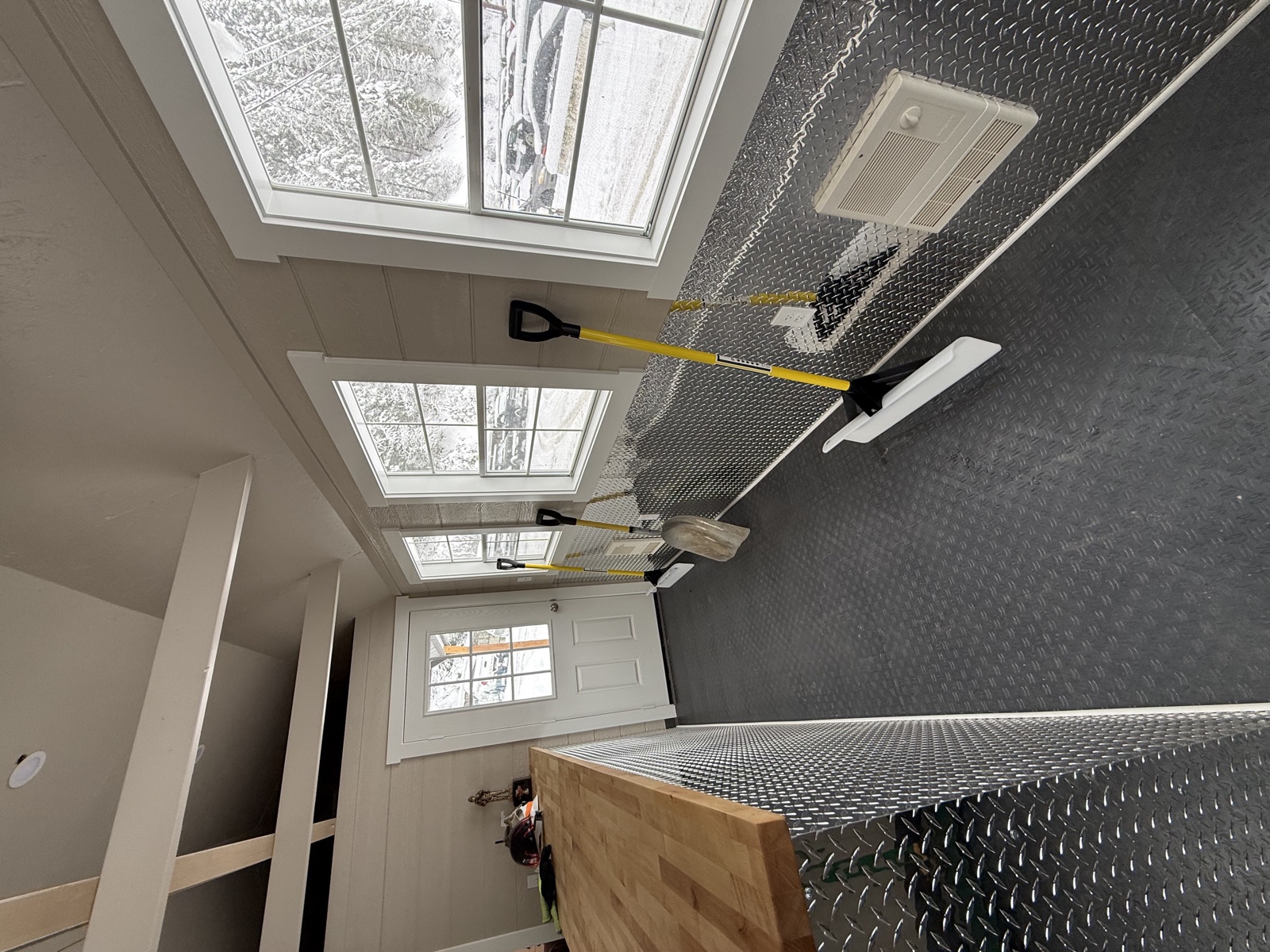 Custom remodel of a guard station with diamond-plate steel walls and floor, twin skylights, a freshly painted white door, and tools staged for the next phase