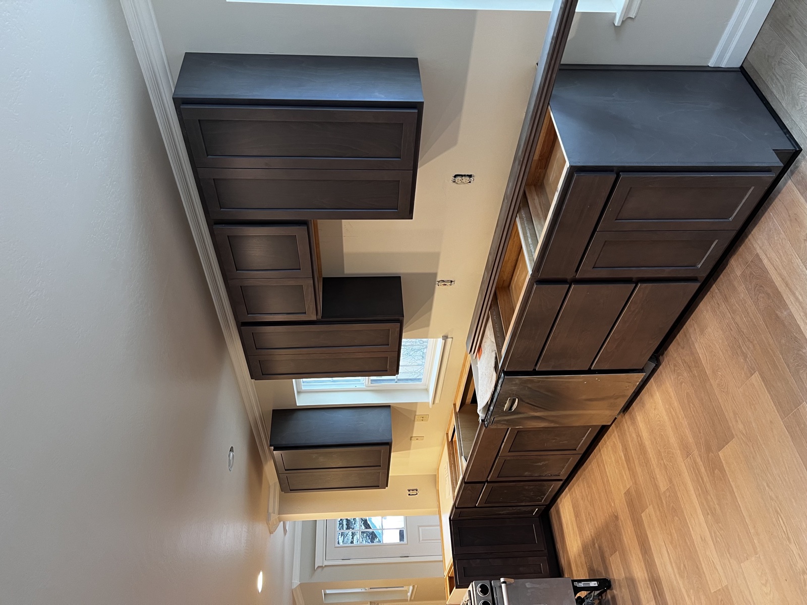 Dark stained custom shaker cabinets installed mid-build, with floating wall cabinets above a base cabinet run in a kitchen still under finish work