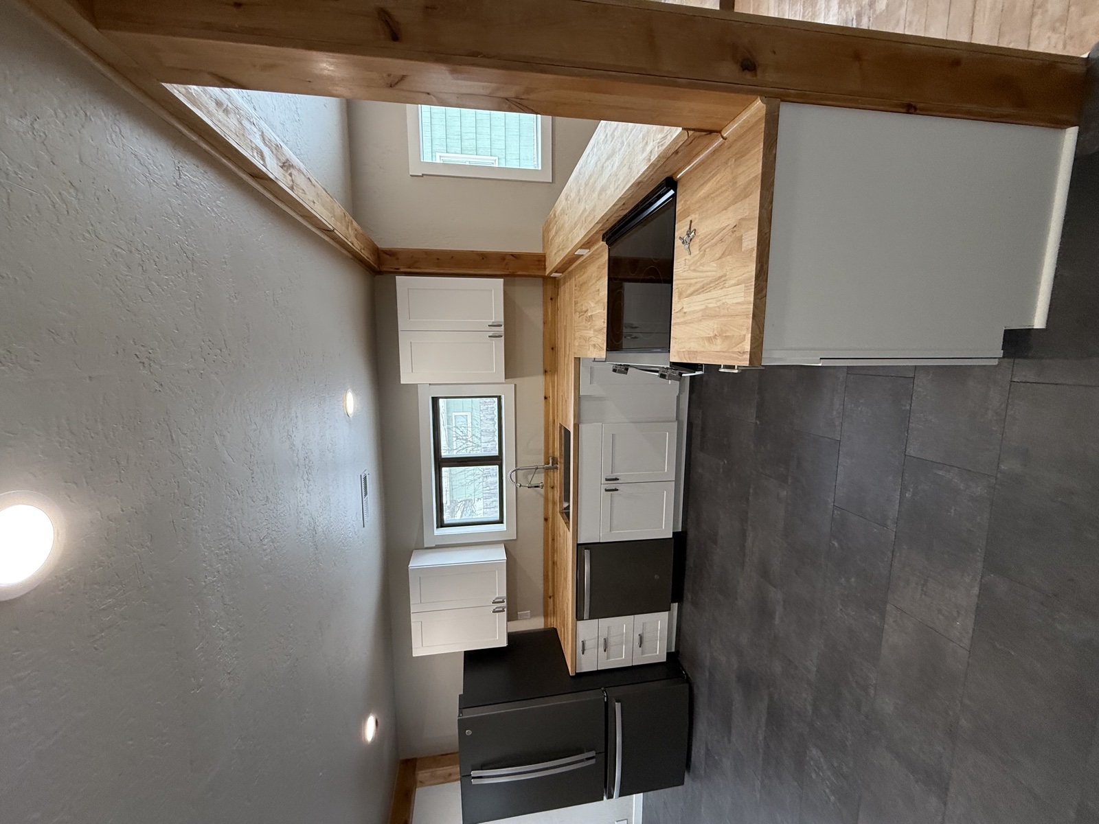 Mountain-modern kitchen with white shaker cabinets, dark slate tile flooring, gray stucco walls, exposed wood beams, stone fireplace mantle, and stainless appliances