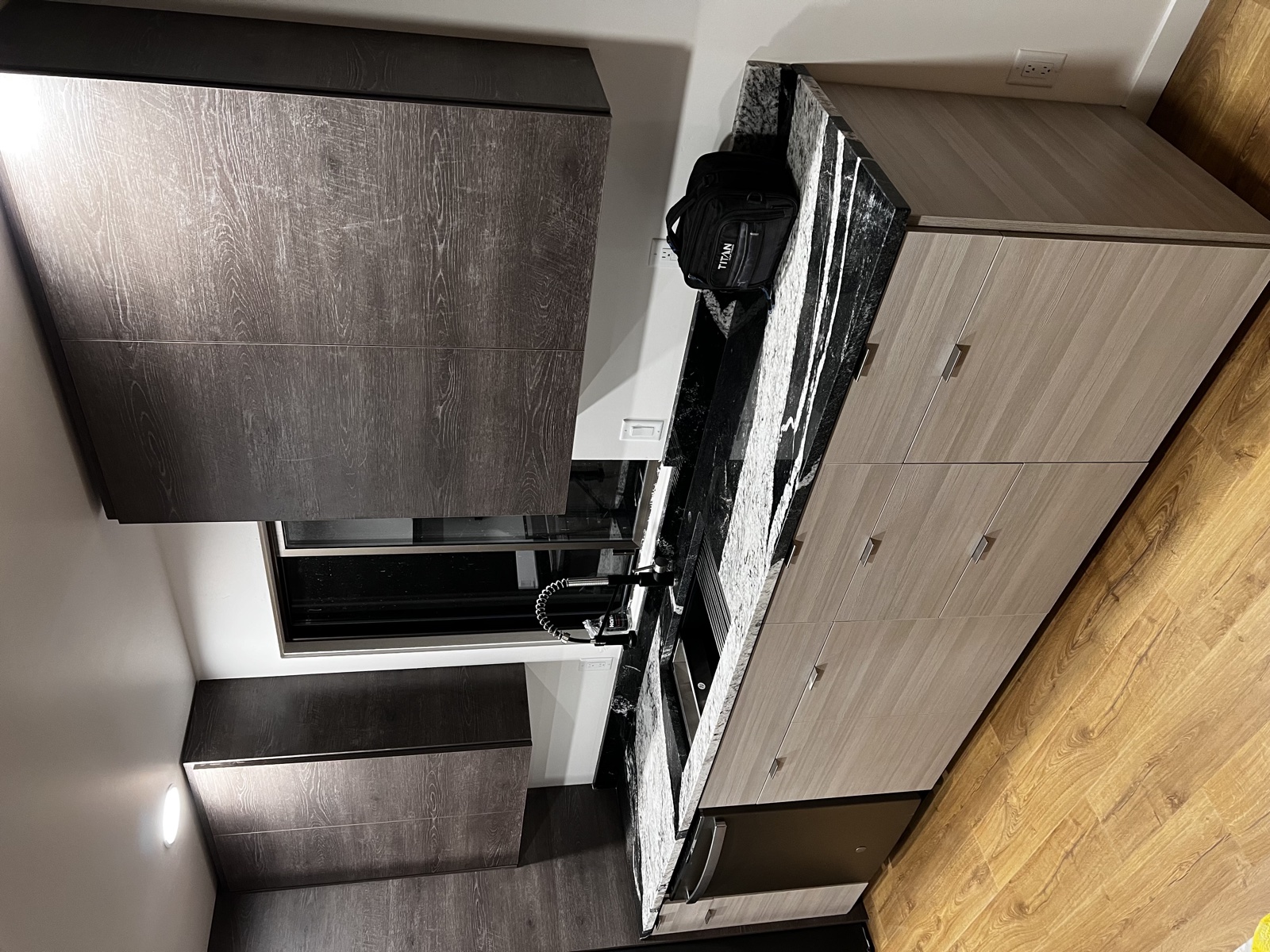 Modern kitchen remodel with dramatic black-and-white marble waterfall island, integrated cooktop, paired dark gray and light gray cabinets, and warm wood floor
