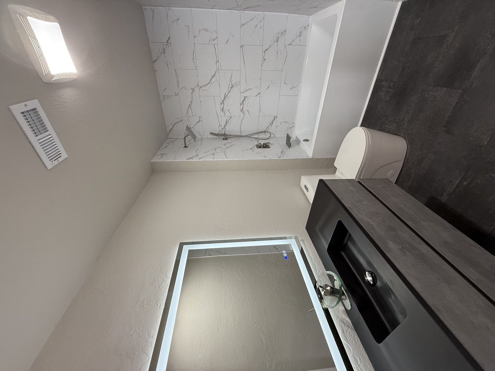 Bathroom finished with light-texture walls, marble tile tub deck, illuminated LED bathroom mirror, walnut vanity, and dark slate floor