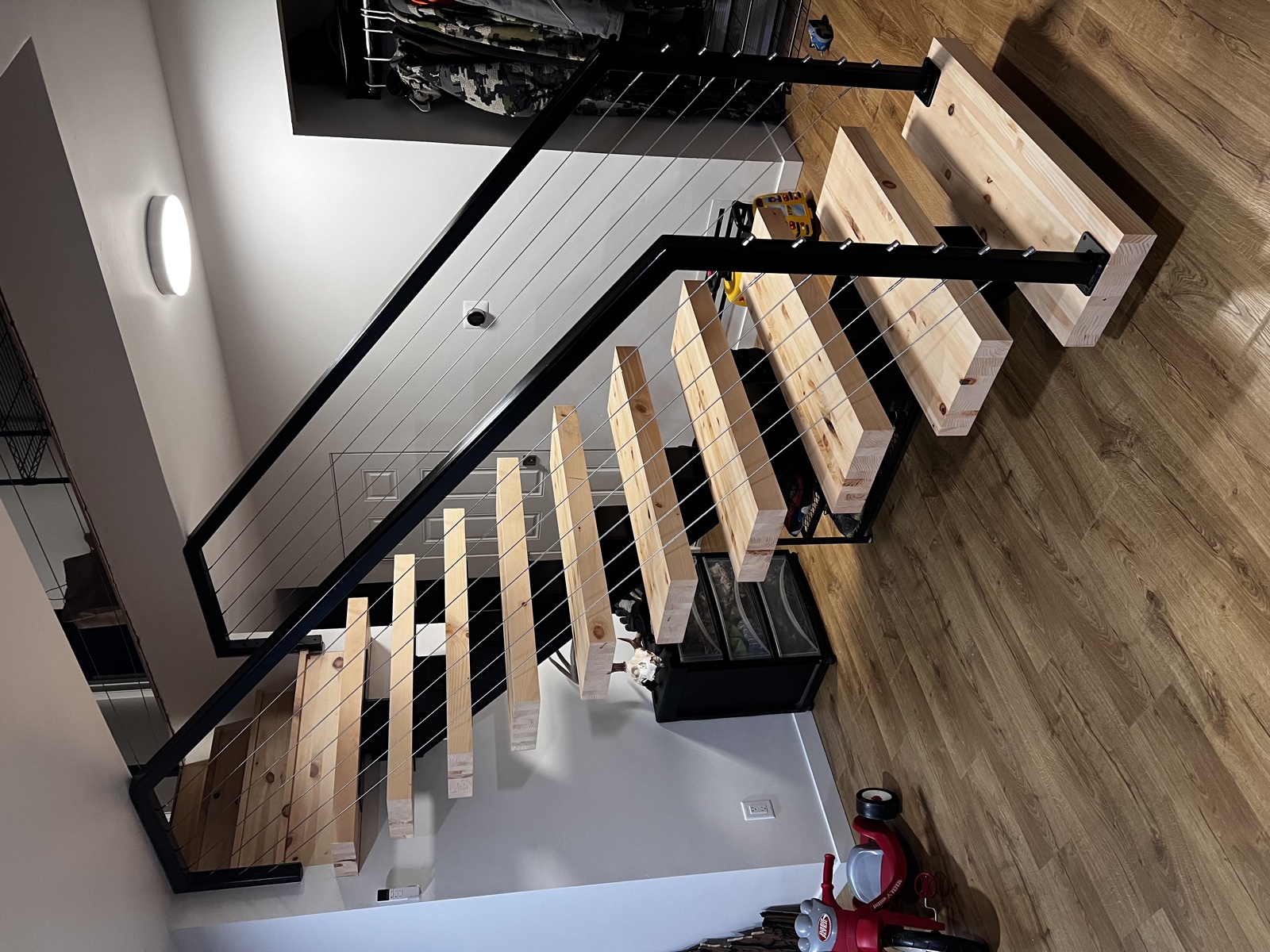Open-tread modern staircase remodel with light wood treads, black steel stringers, horizontal cable railing, and bright white walls